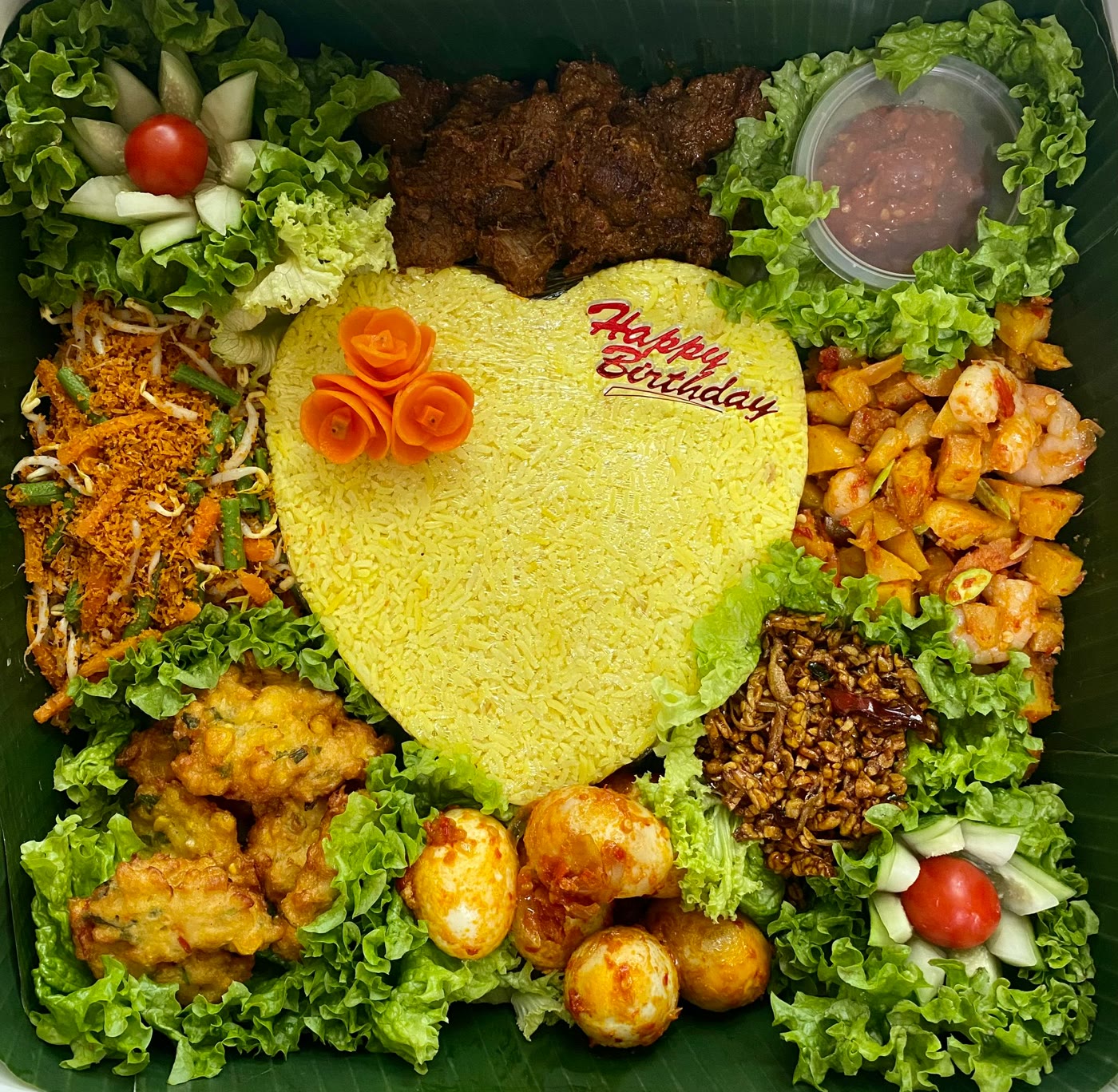 Heart-shaped yellow rice in a box with rendang, urap, corn fritters, eggs and potato with prawn