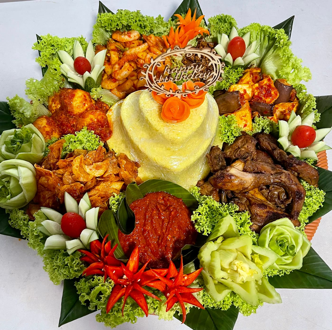 Birthday tumpeng with a heart-shaped yellow rice cone, carved cucumber flowers and chilli blossoms